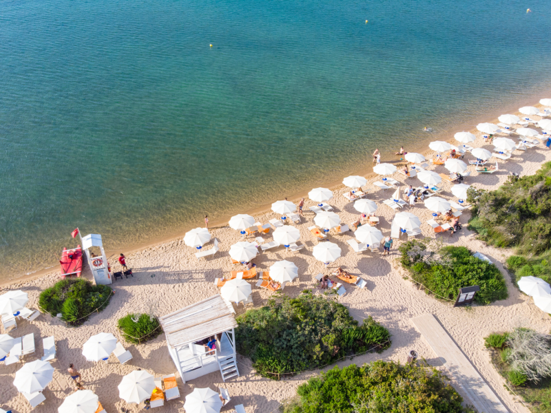 Spiaggia dell'IGV Club Hotel Santaclara in Sardegna con ombrelloni bianchi e acque trasparenti vista dall'alto